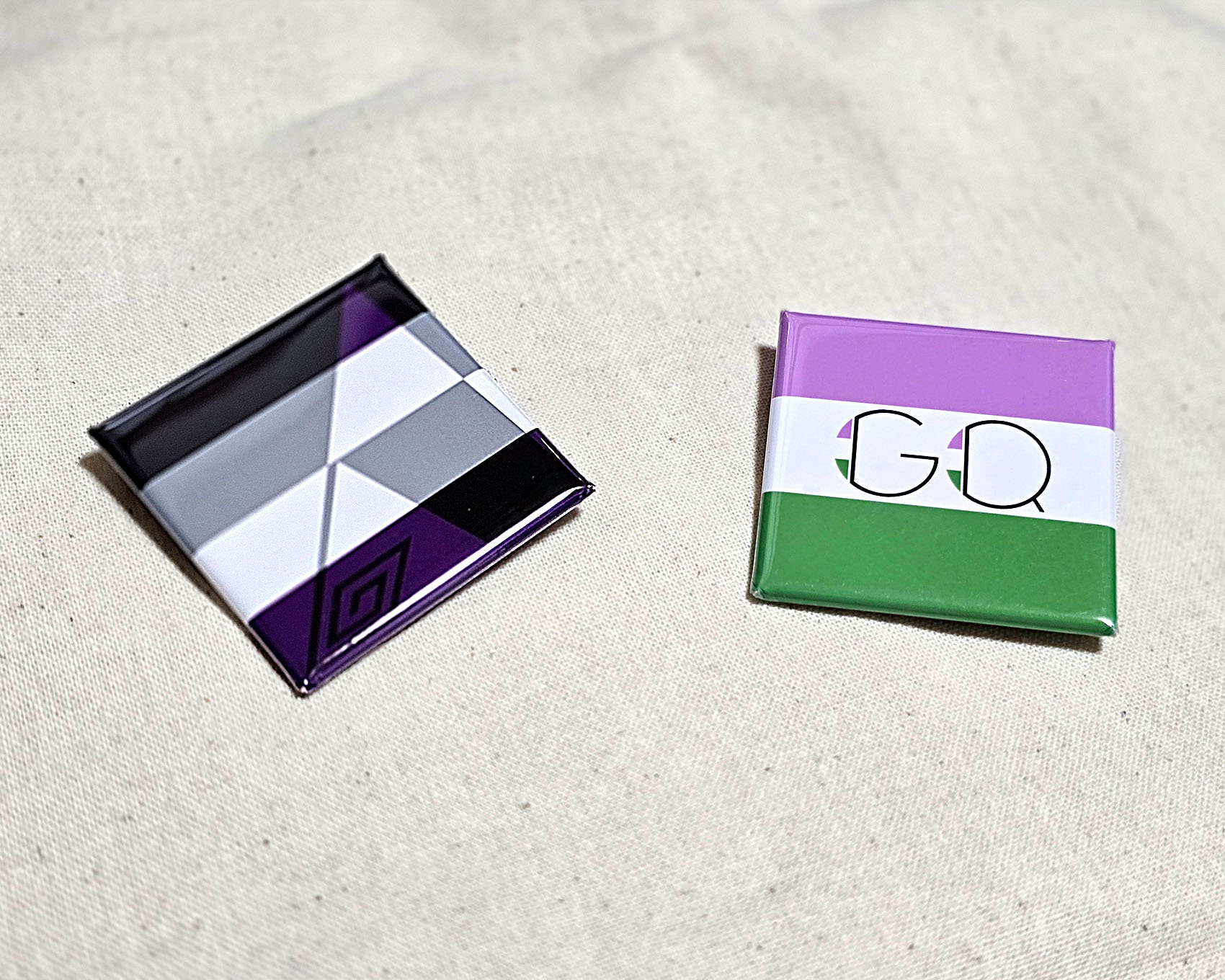 プライドカラー缶バッジの写真。缶バッジが2つ並んでおり、左側にアセクシャルの缶バッジ、右側にジェンダークィアの缶バッジがある。