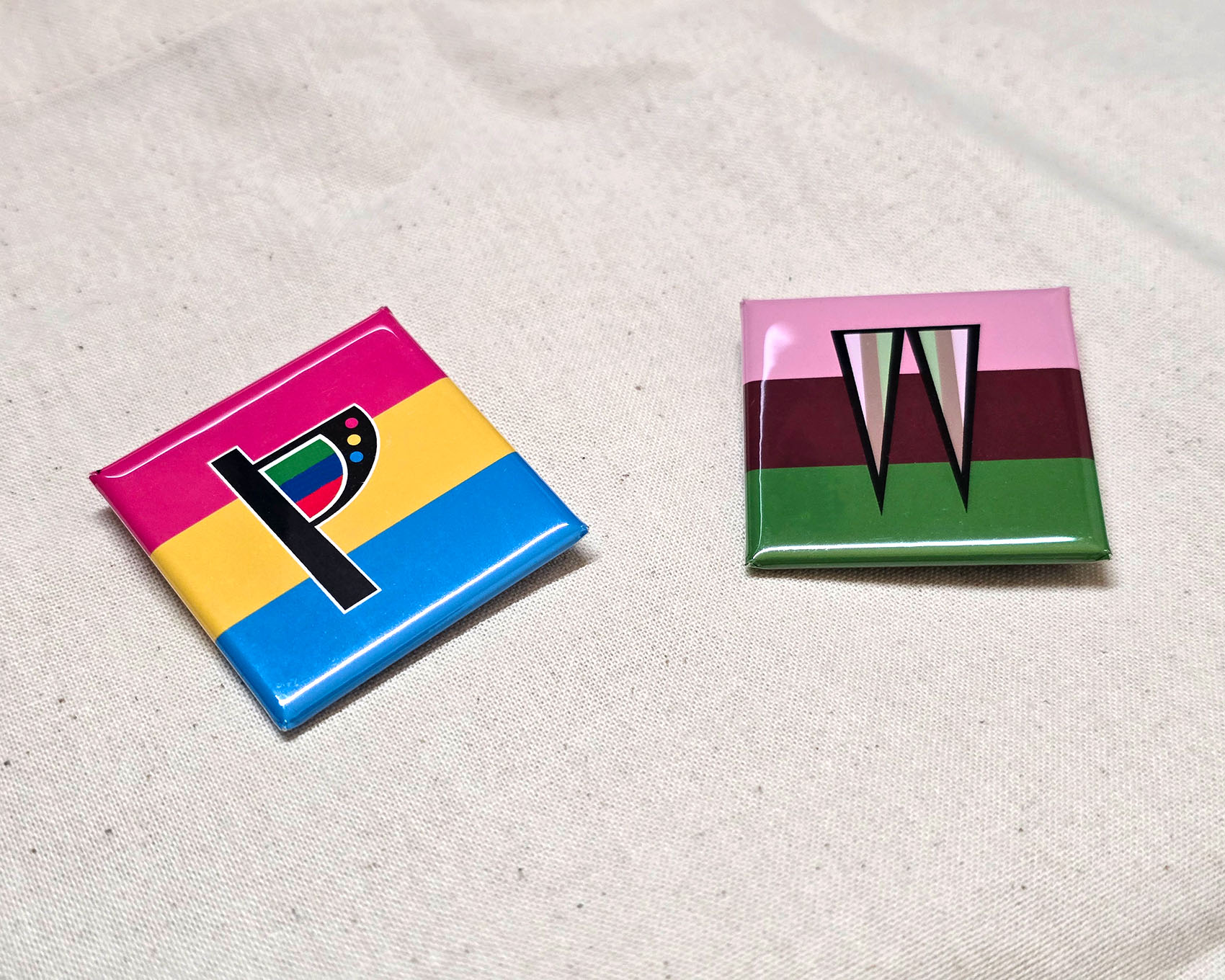 プライドカラー缶バッジの写真。缶バッジが2つ並んでおり、左側にパンセクシャルの缶バッジ、右側にウーマセクシャルの缶バッジがある。