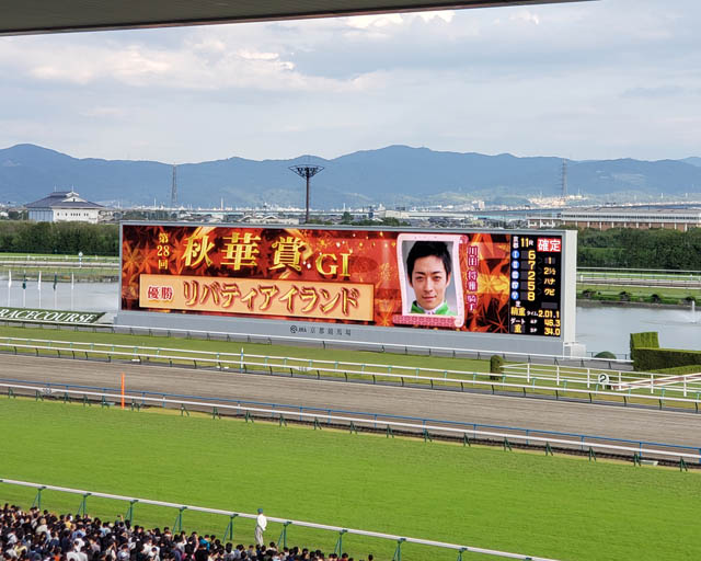 京都競馬場、コース内のスクリーンの画像。「第28回秋華賞 G1 優勝 リバティアイランド」という文字と、川田将雅騎手の顔写真が映し出されている。